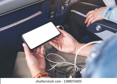 Mockup Image Of Woman's Hand Holding A Black Smart Phone With Blank Desktop Screen And Earphone In Cabin