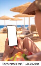 Mockup Image. Woman's Hand Holding Black Mobile Cell Phone With Blank Desktop Screen While Laying Down On Beach. Beach Resort Background. Hand Holding Cellphone With Sea And Beach Blue Sky. Vertical