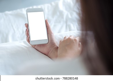 Mockup image of a woman's hand holding white mobile phone with blank desktop screen sitting in the white bed - Powered by Shutterstock