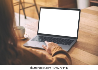 Mockup image of a woman's hand using and touching on laptop touchpad with blank white desktop screen with coffee cup on wooden table 