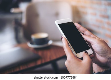 Mockup Image Of Woman's Hands Holding Mobile Phone With Blank Black Desktop Screen In Cafe