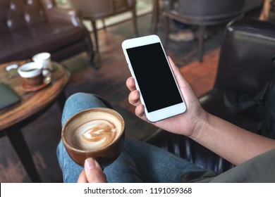 Mockup Image Of Woman's Hands Holding White Mobile Phone With Blank Black Desktop Screen While Drinking Coffee In Cafe