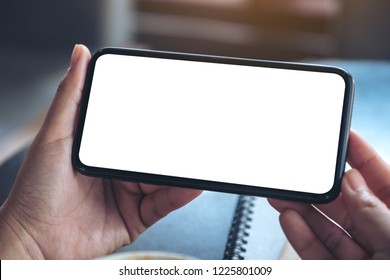 Mockup image of woman's hands holding and using a black mobile phone with blank screen horizontally for watching 