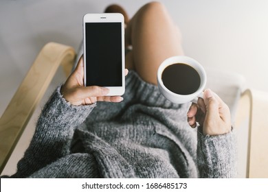 Mockup Image Of Woman's Hands Holding Black Screen Mobile Phone With Blank Screen And Coffee Cup In Her Hand.