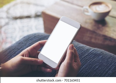 Mockup Image Of Woman's Hands Holding Mobile Phone With Blank White Screen In Vintage Coffee Shop With Green Nature Background