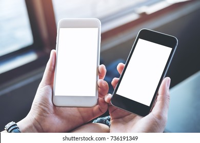 Mockup Image Of A Woman's Hands Holding Two Mobile Phones With Blank White Screen In Modern Cafe