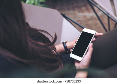 Mockup Image Of Woman's Hands Holding White Mobile Phone With Blank Black Screen On Thigh In Modern Cafe