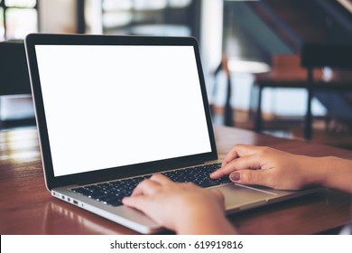 Mockup image of woman's hands using laptop with blank white screen on vintage wooden table in loft cafe