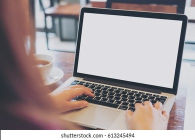 Mockup image of women using laptop with blank white screen on vintage wooden table in loft cafe