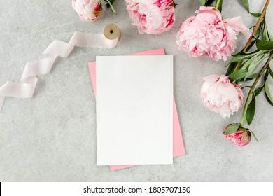 Mockup Invitation, Blank Paper Greeting Card, Pink Envelope And Peonies On Gray Stone Table. Flower Background. Flat Lay, Top View.