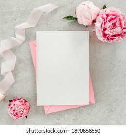 Mockup Invitation, Blank Paper Greeting Card, Pink Envelope And Peonies On Gray Stone Table. Flower Background. Flat Lay, Top View.