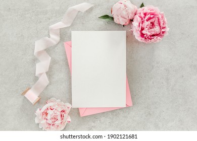 Mockup Invitation, Blank Paper Greeting Card, Pink Envelope And Peonies On Gray Stone Table. Flower Background. Flat Lay, Top View.