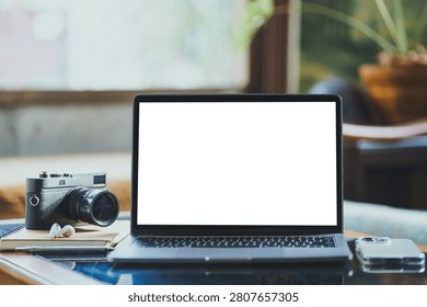 Mockup of laptop computer with empty screen of coffee, modern smartphone, wireless earbuds, notebook, a pen, classic black rangefinder camera morning sunlight.
