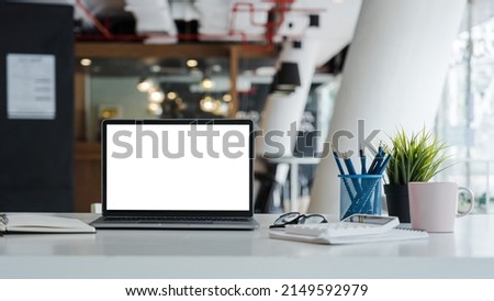 Mockup laptop computer with white screen put on desk table of business office.