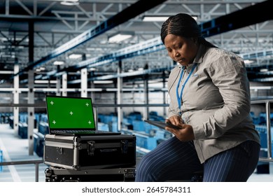 Mockup laptop next to female engineer in server hub using tablet to optimize hardware performance. African american woman in data center using green screen notebook, upgrading rackmounts