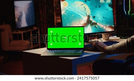 Mockup laptop next to man playing high FPS singleplayer videogame with spaceship shooting laser streams at asteroid. Green screen notebook near gamer using crosshair overlay to hit targets in SF game