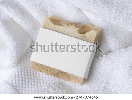 Mockup of light beige solid soap bar with blank paper label on white bath terry towels. Rectangular shape. Unbranded packaging on neutral background with copy space, top view. Personal care context