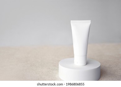 Mockup Luxury Facial Skincare White Tube Bottle Product With Blank Label On White Round Pedestal Or Display Against Sandy White Plain Light Grey Background Copy Space. Minimal Design Concept