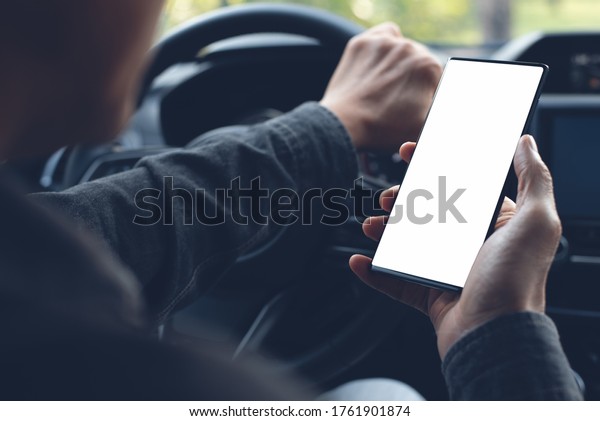 Mockup of man driver hand using\
blank white screen mobile smart phone while driving a car,\
searching location via gps navigator application, close\
up