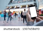 Mockup of man hand using mobile smart phone at shopping center in front of department store for internet payment, digital banking application with blurred crowd people background