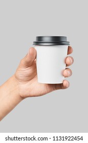 Mockup of men's hand holding white paper cup with black cover isolated on grey background