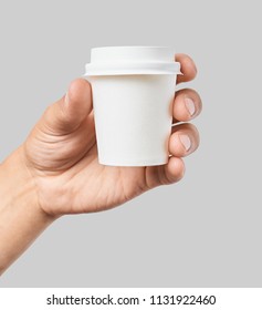 Mockup of men's hand holding white paper cup with white cover isolated on grey background