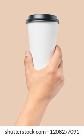 Mockup of men's hand holding white paper large size cup with black cover isolated on orange background