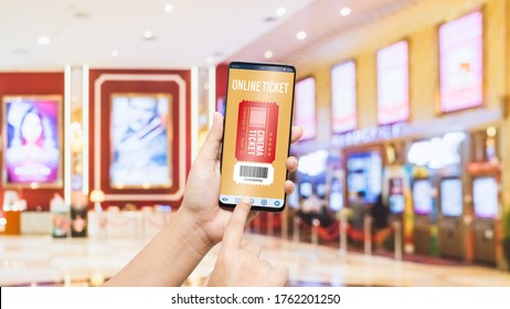 Mockup Mobile Phone Hand Using Smartphone To Buy Cinema Tickets With Blurred Image Of Ticket Sales Counter At Movie Theater With Graphic Icon, Online Booking And Payment Concept