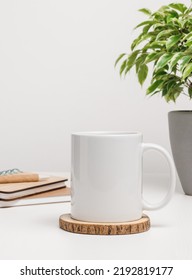 Mockup mug with notepads and houseplant at the background. Mug with copy space for logo and brand, mug for the office or education