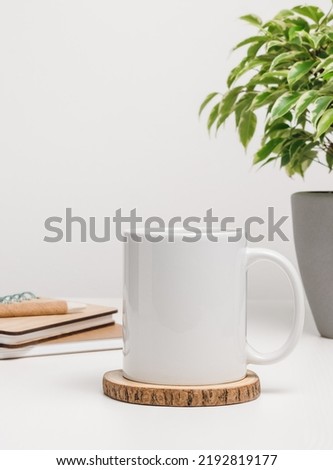 Mockup mug with notepads and houseplant at the background. Mug with copy space for logo and brand, mug for the office or education
