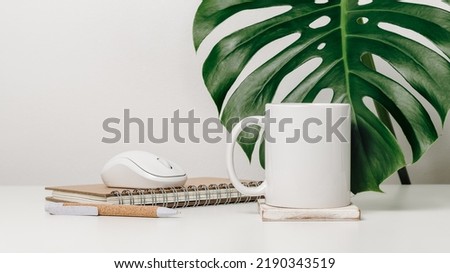 Mockup mug with office objects at the background and monstera leaf. Mug with notepad and pen for brand logo, design or text
