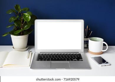 Mockup Of Open Laptop Computer With Blank Copy Space Screen For Your Text Or Promotional Content. White Table With Generic Notebook, Mobile Phone, Decorative Plant, Stationery Items And Mug Of Coffee