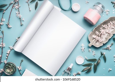 Mock-up of open magazine or catalog for beauty and cosmetic products on pastel blue desktop with twigs and cherry blossom. Modern spring skin care concept, top view, flat lay