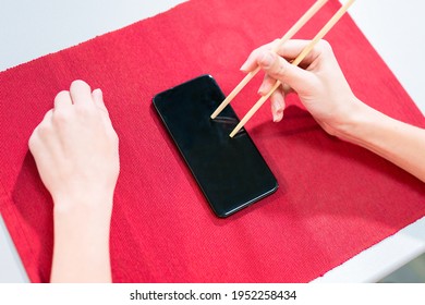 Mockup For Ordering Japanese And Oriental Cuisine Online: Hand Holding Chopsticks And Smartphone Screen