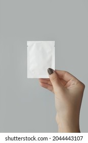 Mockup Of Packaging Sachet Bag For Small Volume Of Cosmetics In Female Hand On Gray Background