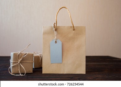 Mockup Paper Bag From Kraft Paper With Gift Tag And Christmas Gift Boxes On A Wooden Background