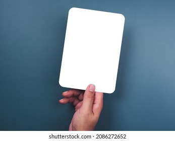 Mockup Paper Holding With The Right Hand. Hand Holds The White Blank Mock-up White Paper With A Rounded Corner And A Vertical Style On A Blue Background.