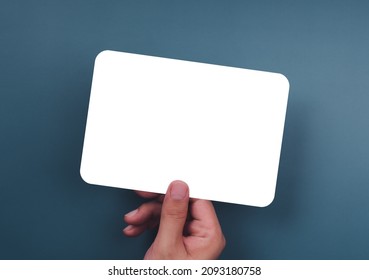 Mockup Paper Holding With The Right Hand. Hand Holds The White Blank Mock-up White Paper With A Rounded Corner And A Horizontal Style On A Blue Background.