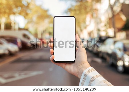 Mockup of a phone held by a woman's hand on the street. Blank screen to insert design. Front view
