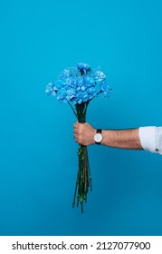 Mockup Photo Of Male Hand With A Fresh Bouquet Of Blue Flowers Isolated On Blue Background. Birthday. Women's Day. Valentine's Day. Holidays Presents.