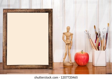 Mockup picture frame with wooden doll, red apple and box of brushes on wooden table - Powered by Shutterstock