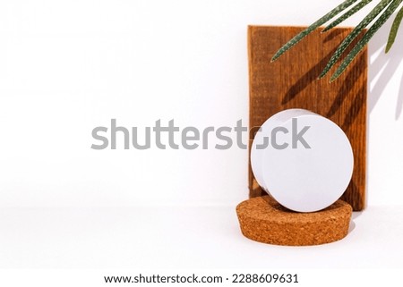 Mockup of round box for beauty product on cork stage and aloe plant. Branch or tree root and wooden plank in background. White backrop. Free spase for text.