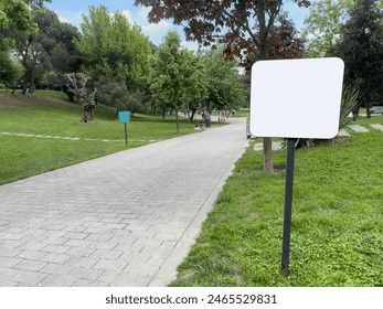 mockup, side view Empty or Blank White Signpost by path in park in spring or summer. Blank white board for information and indications in park, with a background of green grass and tree