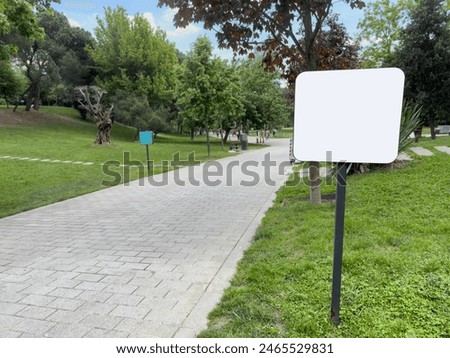 mockup, side view Empty or Blank White Signpost by path in park in spring or summer. Blank white board for information and indications in park, with a background of green grass and tree