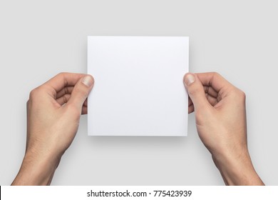 Mockup Square Empty Blank White Postcard Holds The Man In His Hand. Isolated On A Gray Background