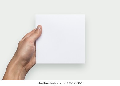 Mockup Square Empty Blank White Postcard Holds The Man In His Hand. Isolated On A Gray Background