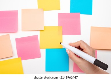 Mockup Sticky Note Paper. Many Colored Empty Sticker Notes On White Wall. Hand With Black Marker Ready To Write. Blank Sticker Notes On White Background. Empty Sheets For Notes On Bulletin Board