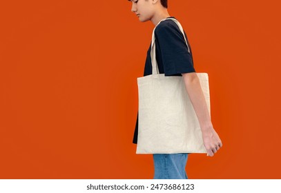 Mockup teen boy carry blank cotton canvas bag with no logo, possible for logo design. A person with reusable shopping bag isolated on colorful background.