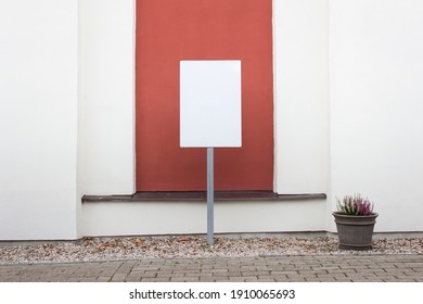 Mockup template with empty information board next to building wall with red color accents and potted plant.