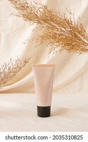 Mockup tonal CC or BB cream foundation makeup beige plastic tube mockup on linen drapery and dry plant. Concept eco organic cosmetic with natural extract. Mockup skincare cosmetic product